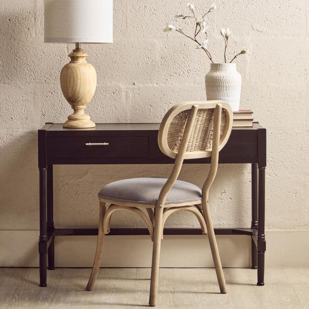 Wooden desk with a chair and decorative items against a beige wall.