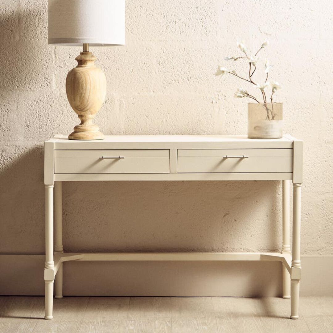White console table with a lamp and decorative vase against a textured wall.