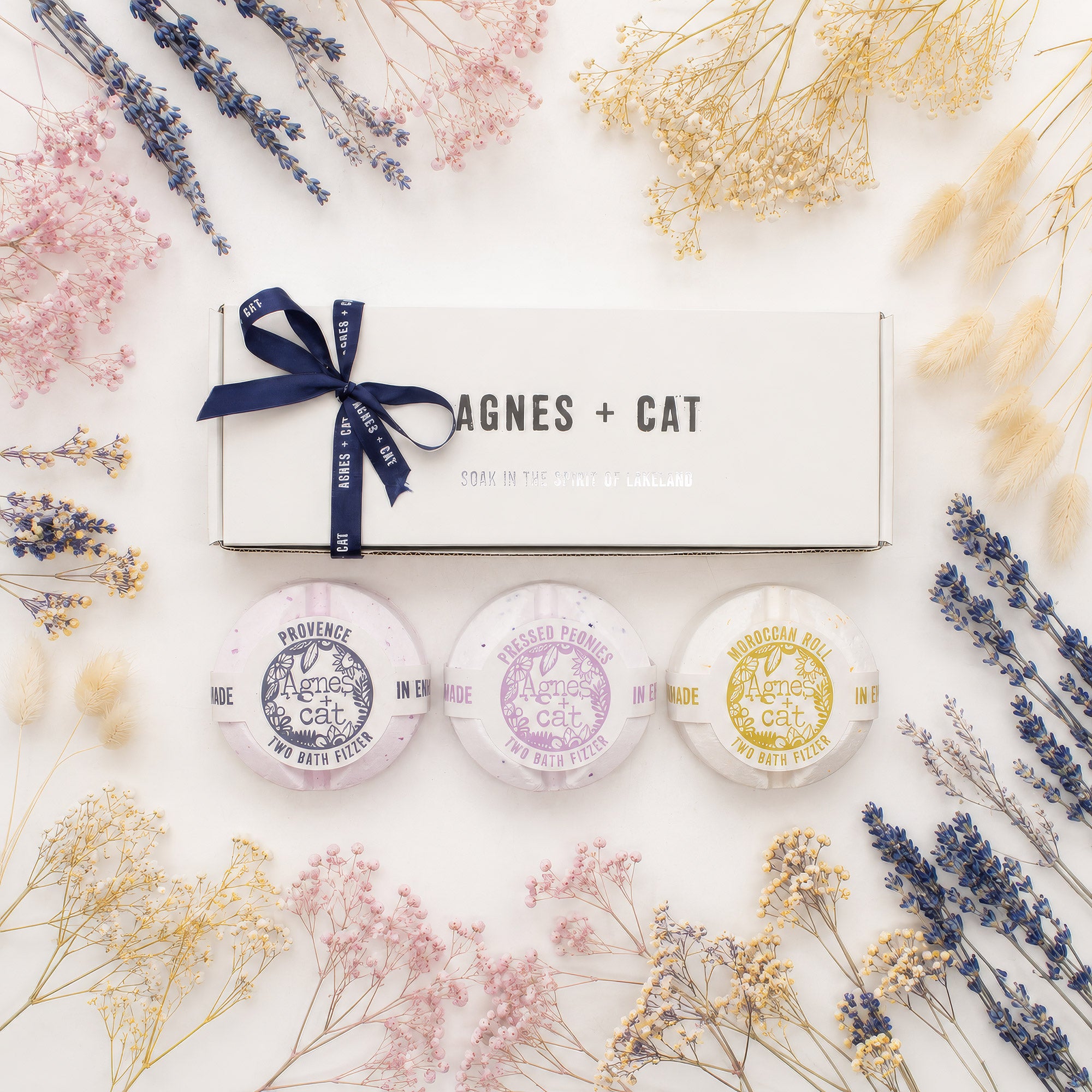 Set of three small containers with decorative labels on a white surface with dried flowers.
