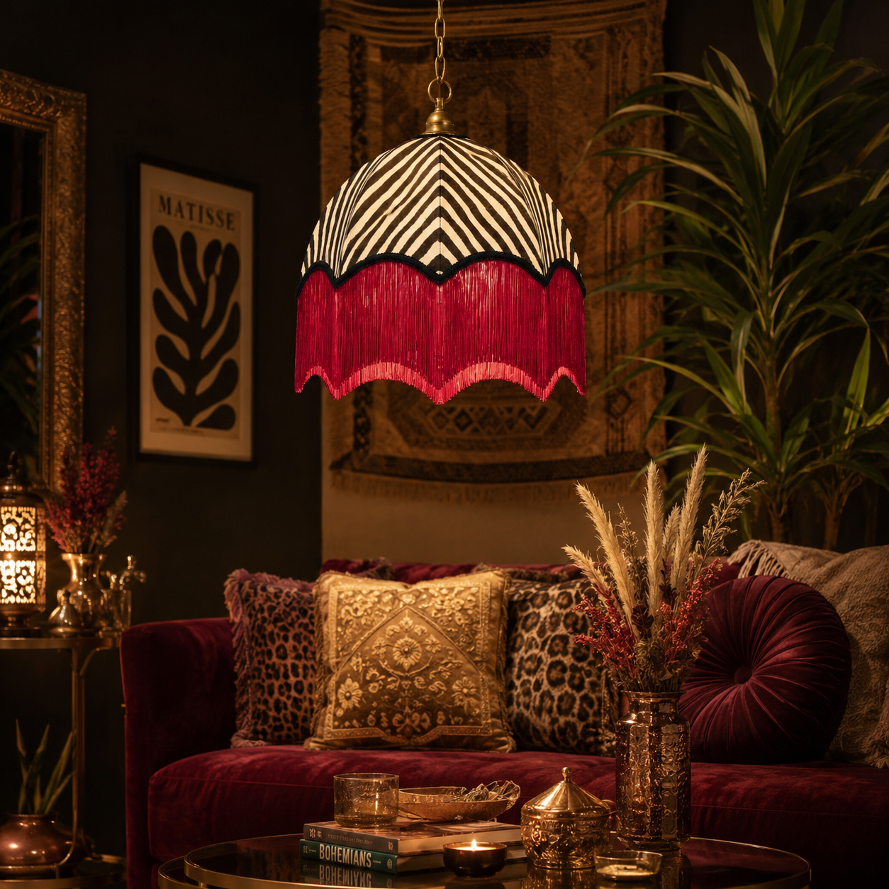 A bohemian-style pendant lamp with a black and white zebra-patterned shade and a deep magenta fringe, hanging in a dark, richly decorated living room over a velvet red sofa.