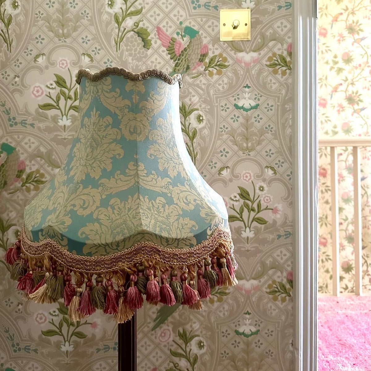Decorative lampshade with tassels on a floral wallpapered wall.