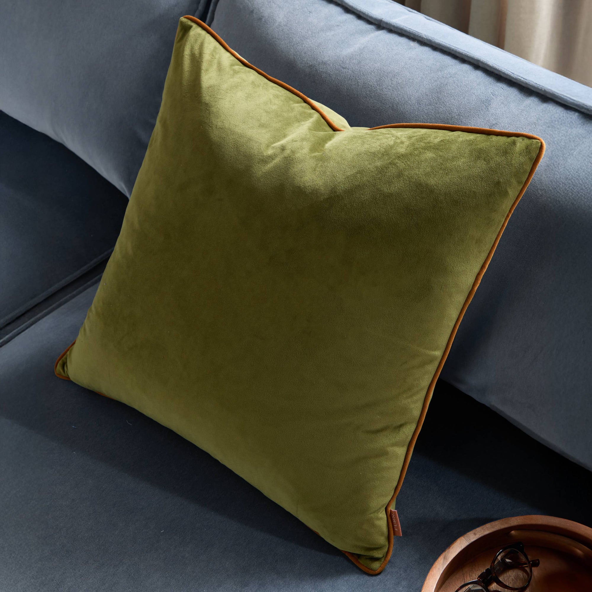 Green pillow with brown trim on a gray sofa