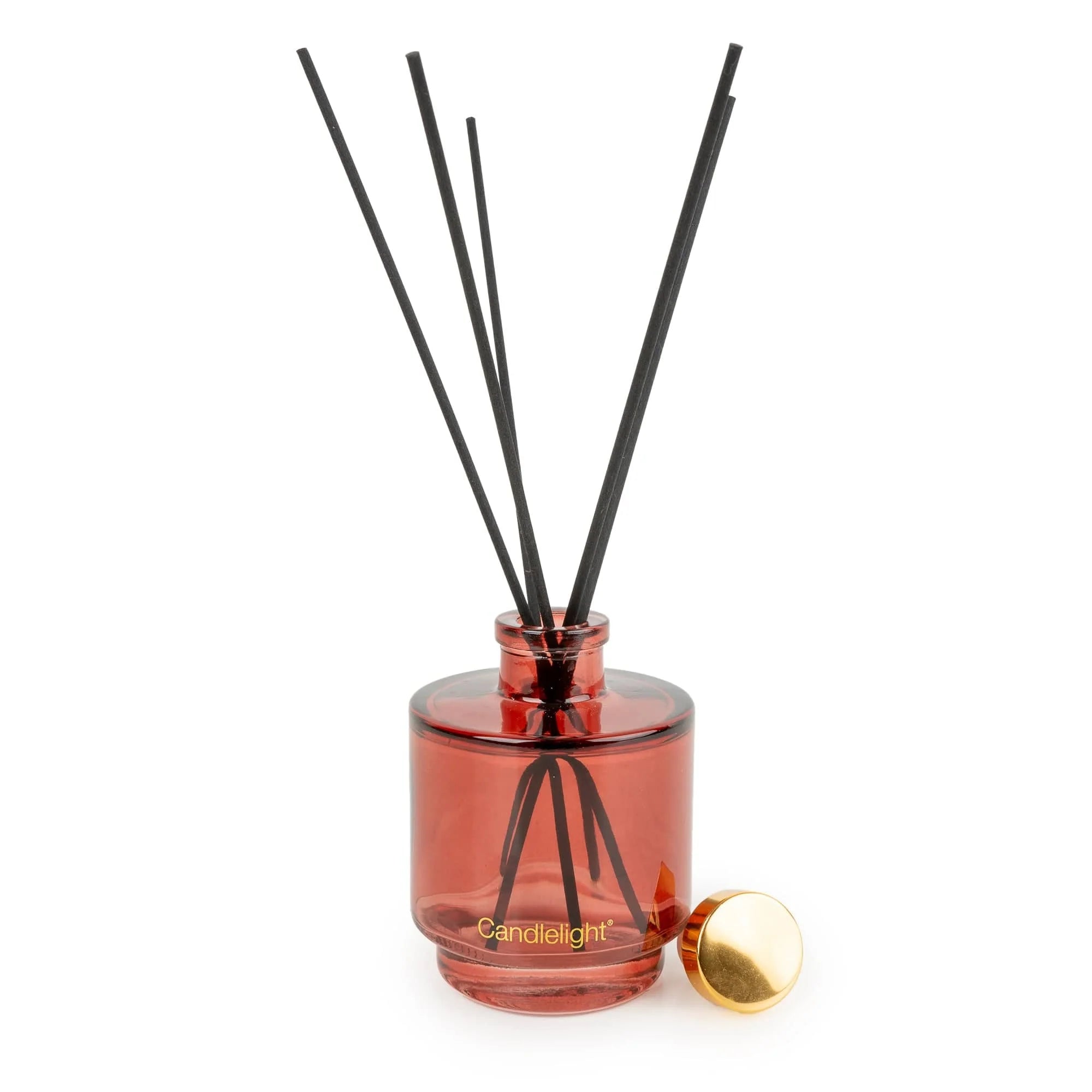 A reed diffuser bottle in translucent amber-red glass with black reeds and a small gold cap resting beside it on a white background. The brand name 'Candlelight' is printed in gold near the base.