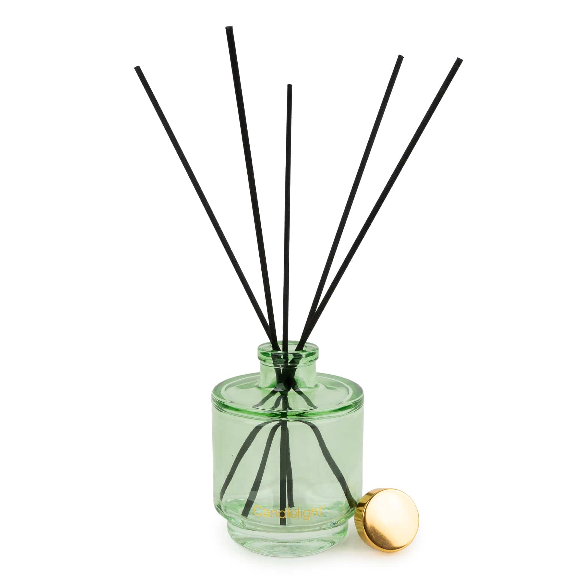 A green glass reed diffuser bottle with black reed sticks and a small gold cap resting beside it on a white background.
