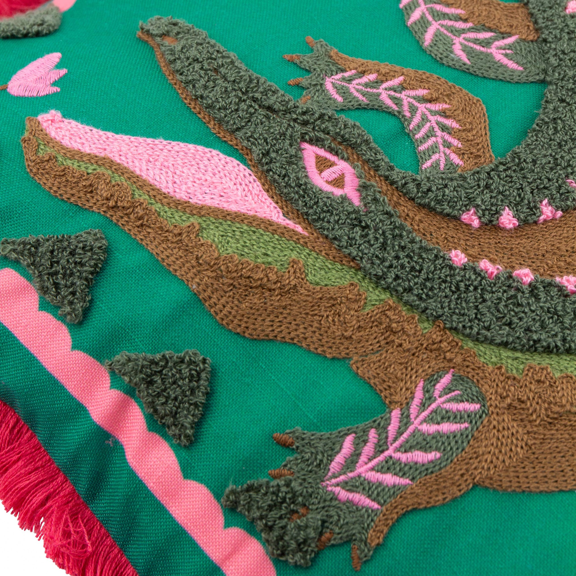 Close-up of embroidered fabric with green, brown, and pink leaves on a teal background.