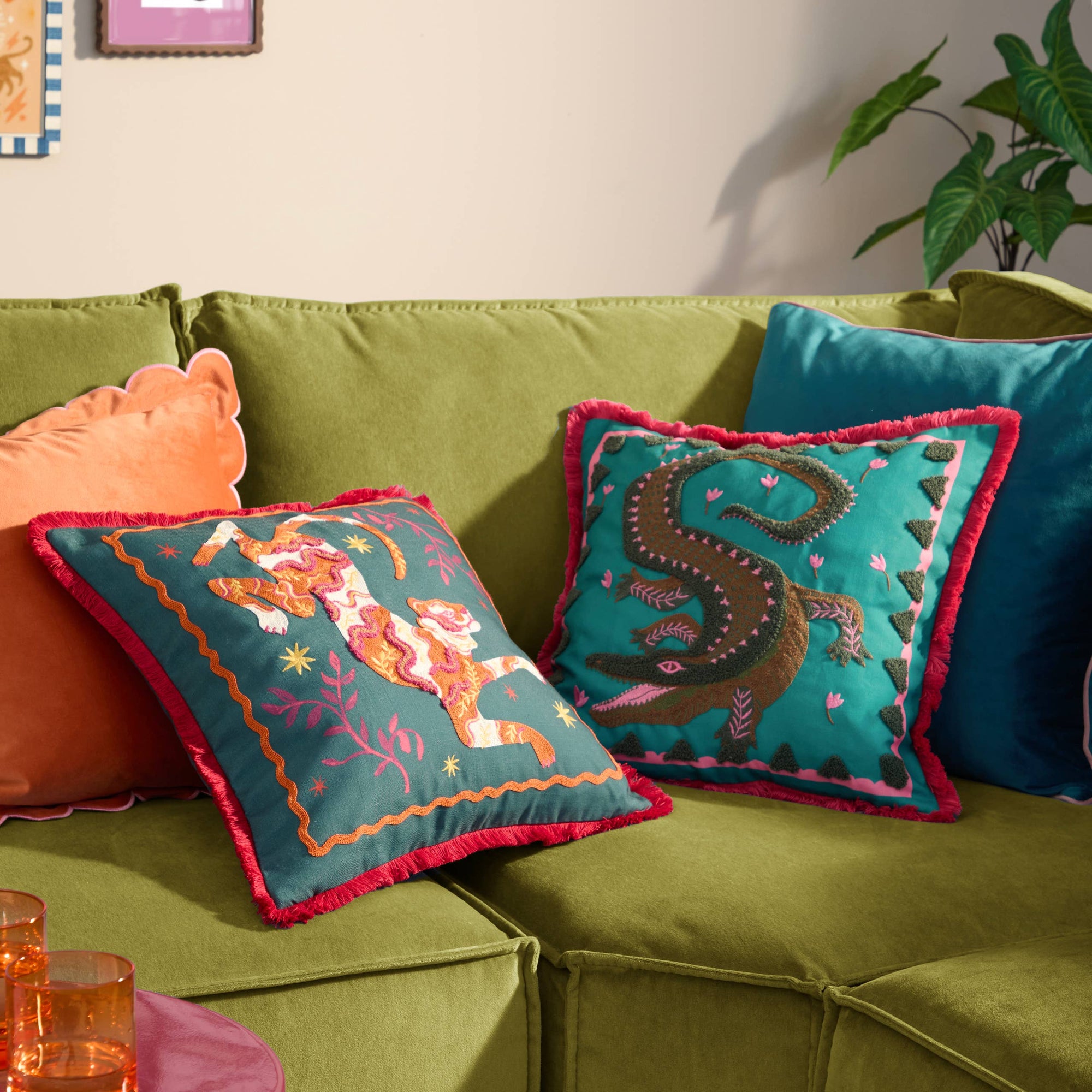 Colorful embroidered cushions on a green sofa with a plant in the background