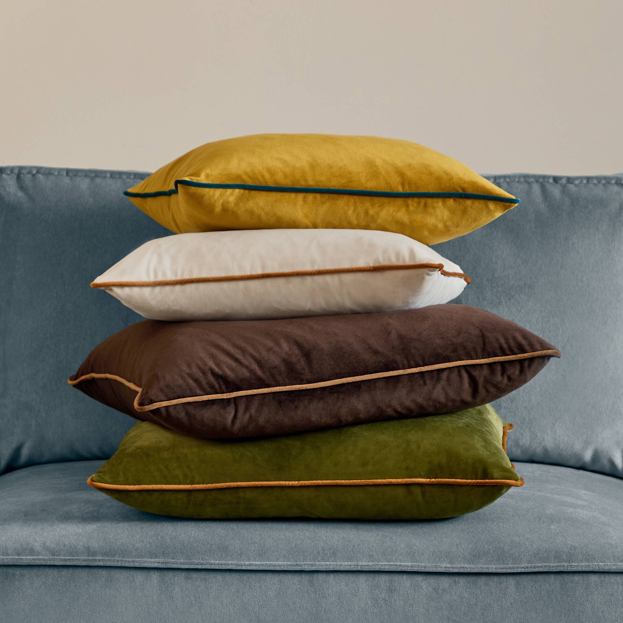Stack of colorful pillows on a blue sofa against a beige wall