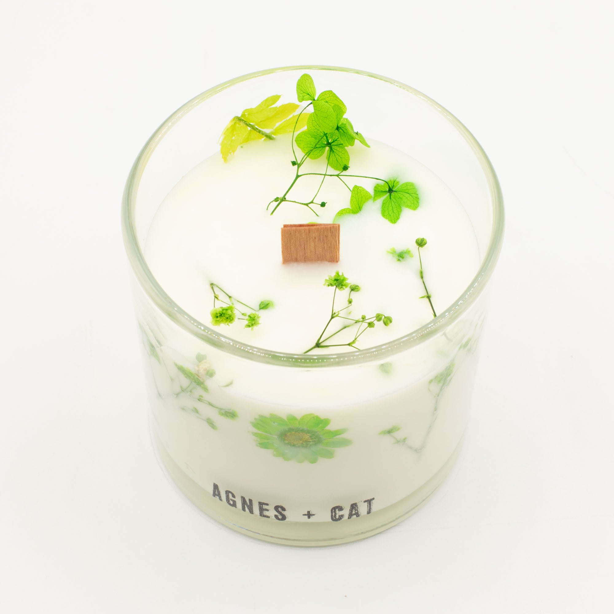 Candle in a glass jar with greenery and 'AGNES + CAT' branding on a white background