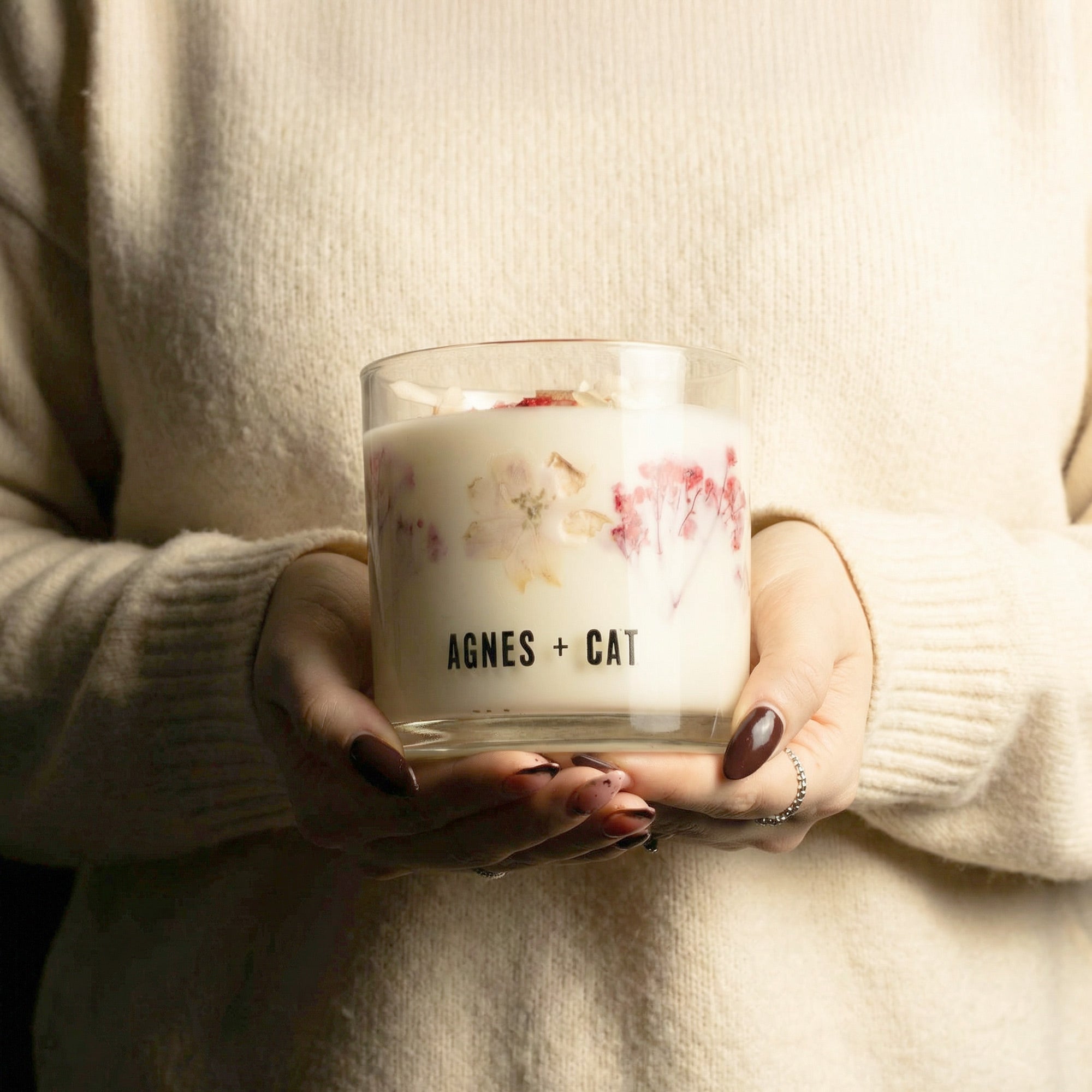 Person holding a 'AGNES + CAT' candle in a warm setting