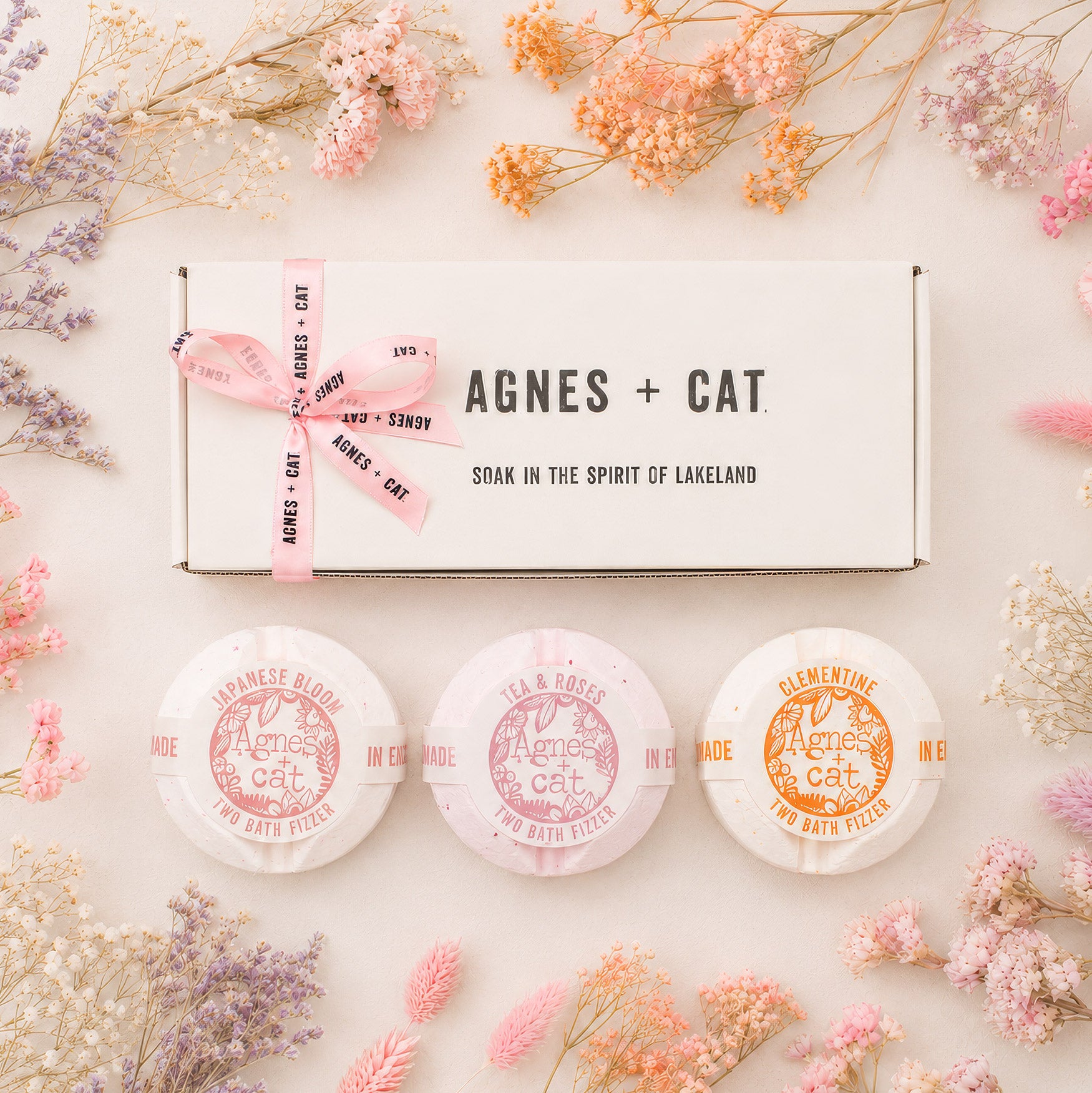 Three bath bombs with 'Agnes + Cat' branding surrounded by dried flowers on a light background.
