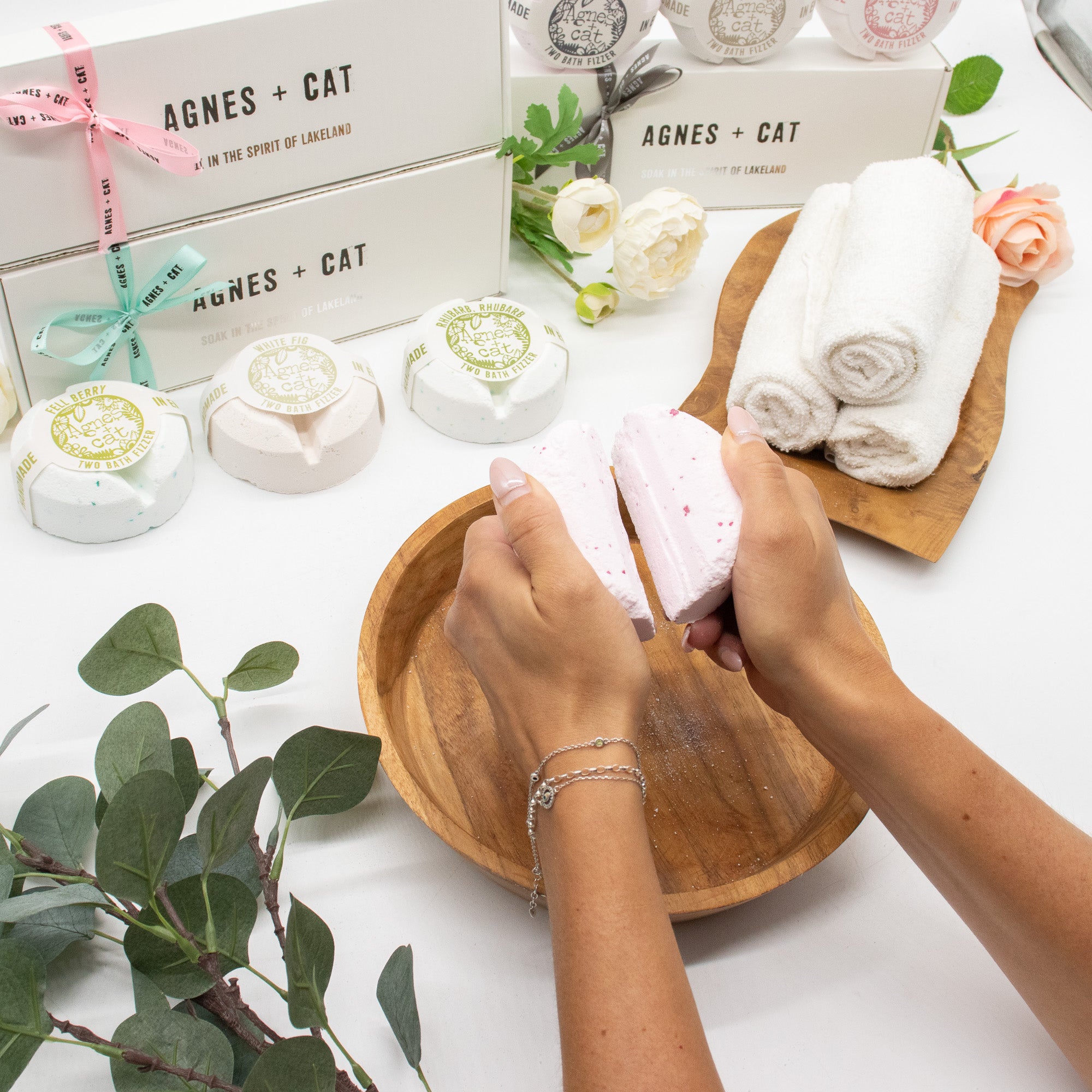 Person holding a pink soap bar in a wooden bowl with 'Agnes + Cat' products in the background.