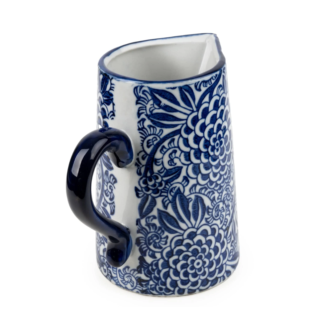A small ceramic pitcher with a dark blue floral pattern on a white background, featuring a dark blue handle and rim, photographed on a clean white background.