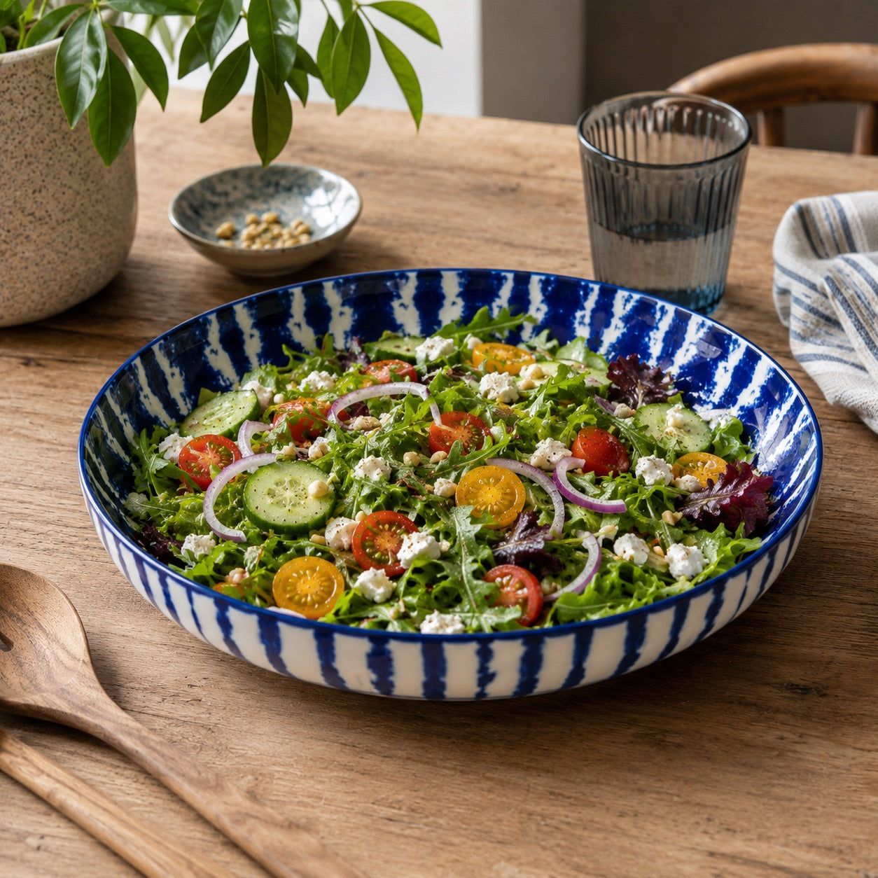 A large ceramic salad bowl with a blue and white striped pattern, filled with a fresh green salad, set on a rustic wooden dining table.