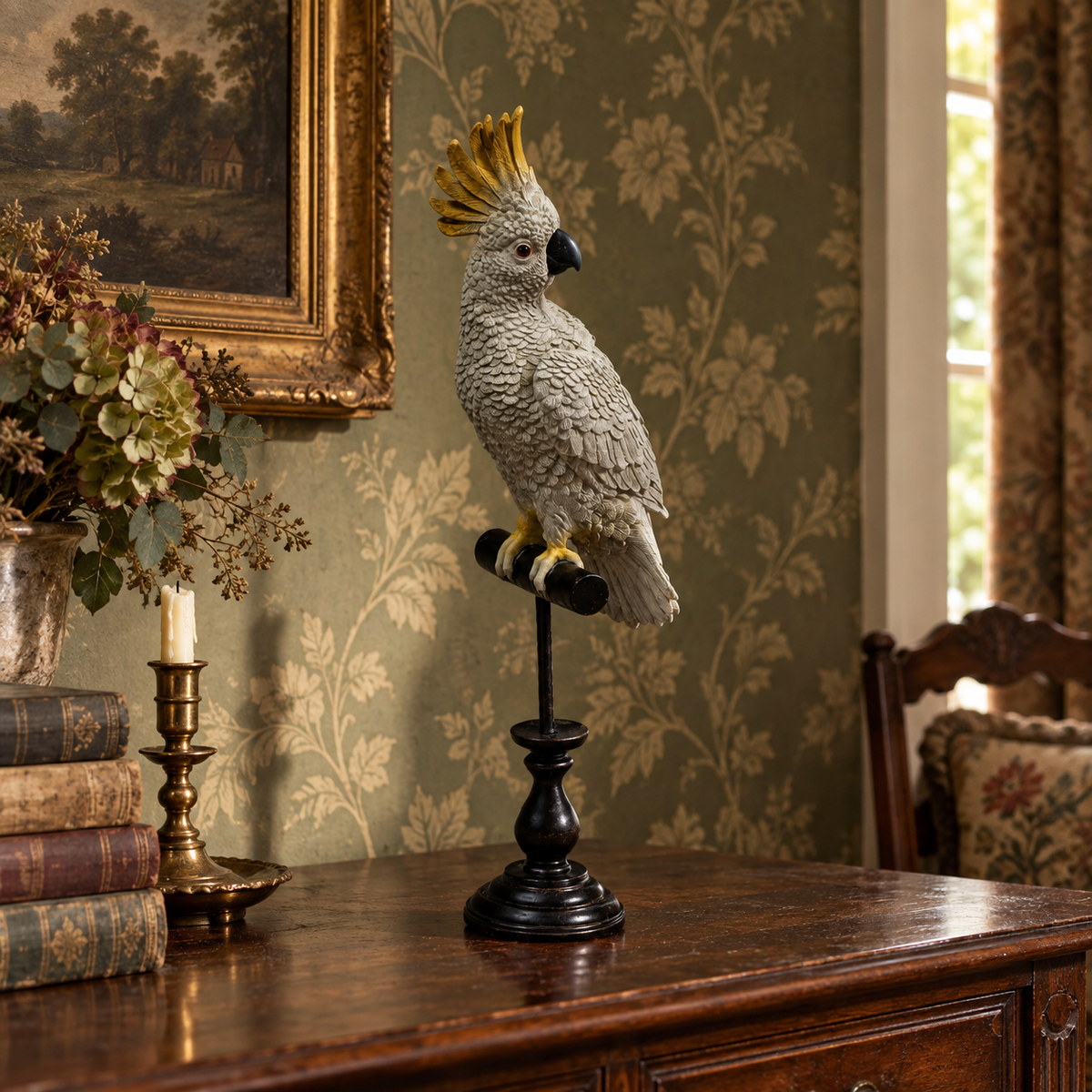 A decorative cockatoo figurine with a yellow crest perched on a black stand, displayed on a wooden cabinet in a vintage-style room with floral wallpaper, framed art, and a candlestick.