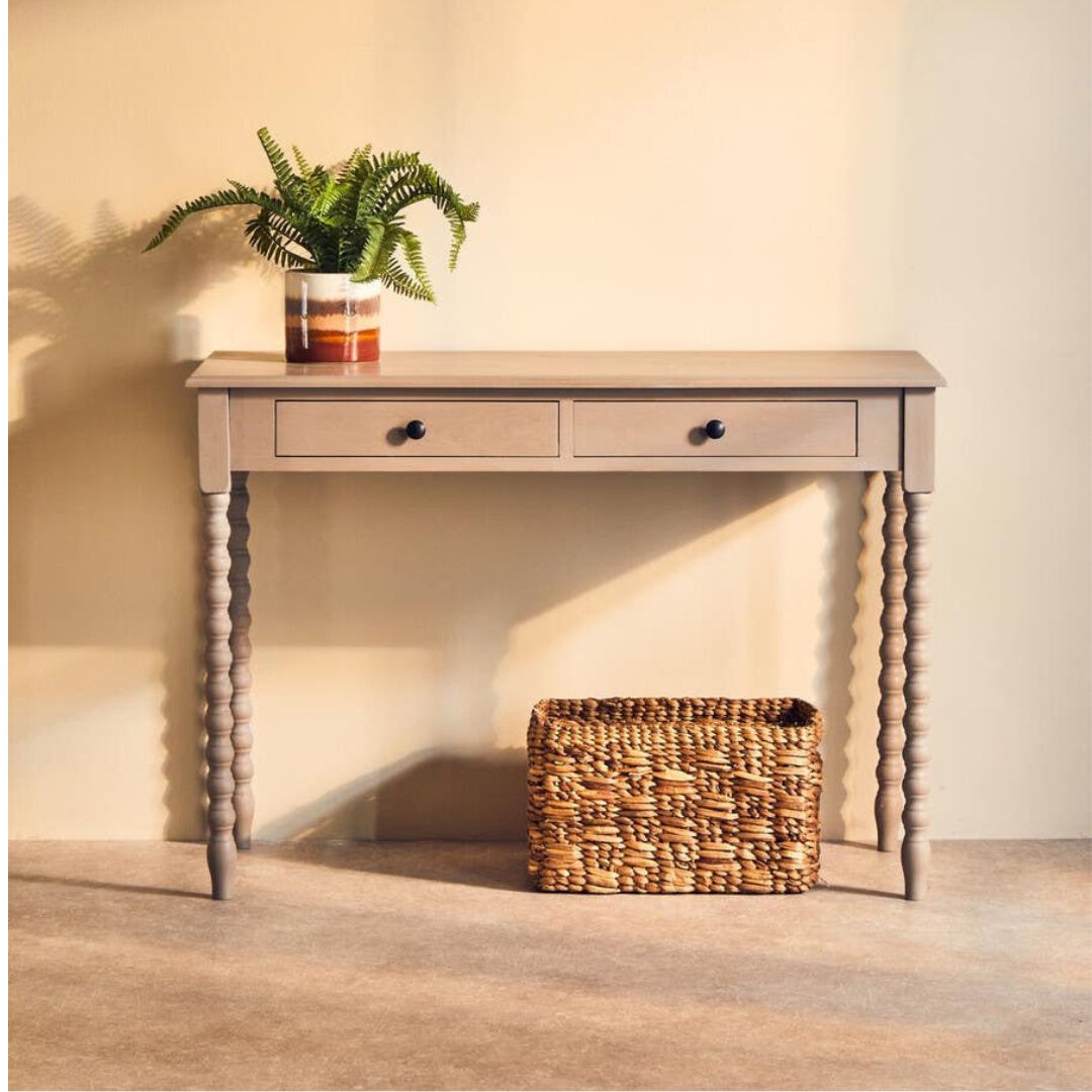 Wooden console table with a plant and woven basket against a beige wall.