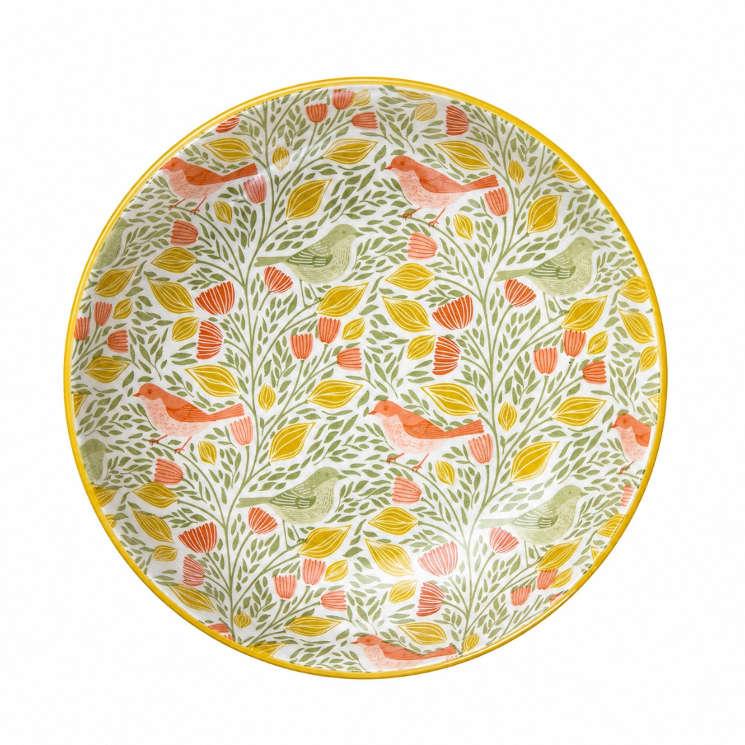 A round ceramic plate featuring a dense botanical pattern of orange birds, green leaves, and yellow-orange flowers on a white background, finished with a yellow-gold rim.